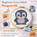 Cute penguin beginner counted cross stitch kit with finished design in embroidery hoop, floss, Aida fabric, and pattern chart.